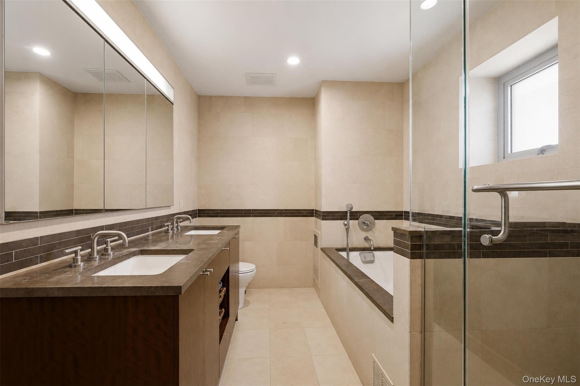 Bathroom featuring a dual vanity with integrated sinks, a built-in soaking tub, and a separate glass-enclosed shower