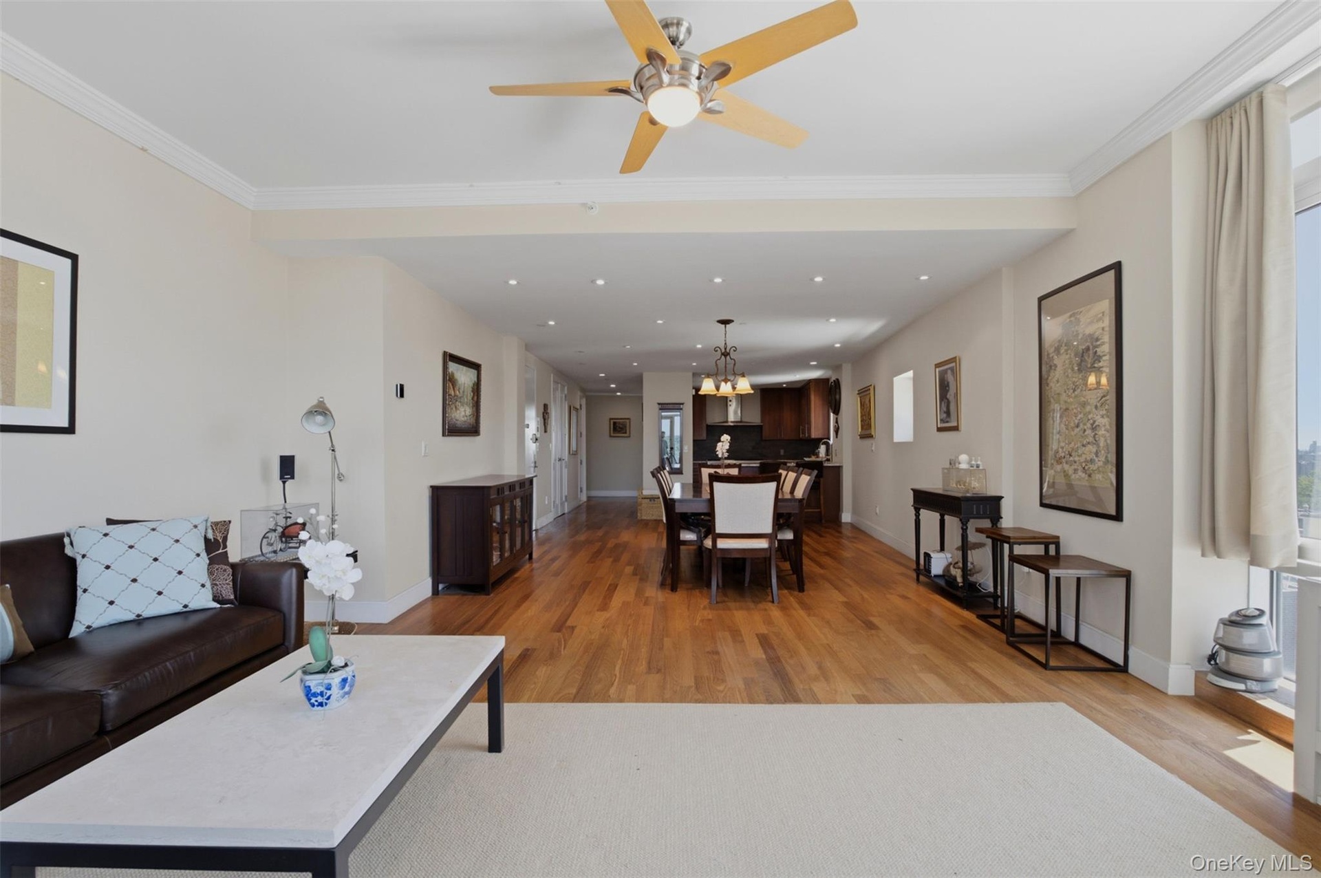 Expansive open-concept living area featuring wood-finish flooring, a ceiling fan, recessed lighting, and crown molding