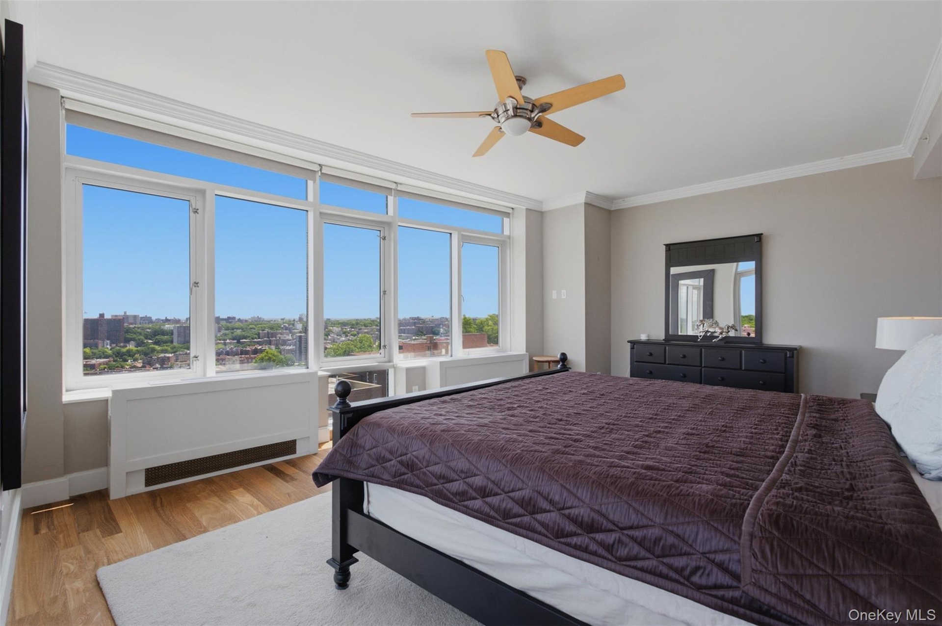 Primary bedroom featuring extensive window line, wood-finish flooring, and crown molding