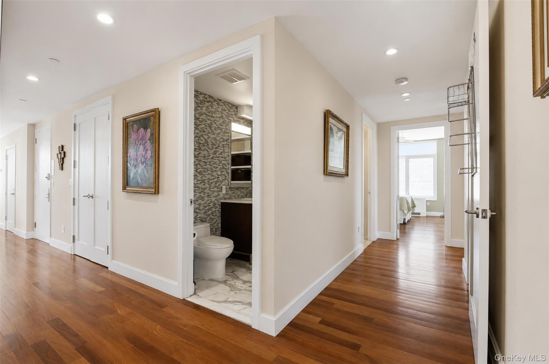 Hardwood flooring extends throughout this interior hallway, featuring recessed lighting and a white trim package