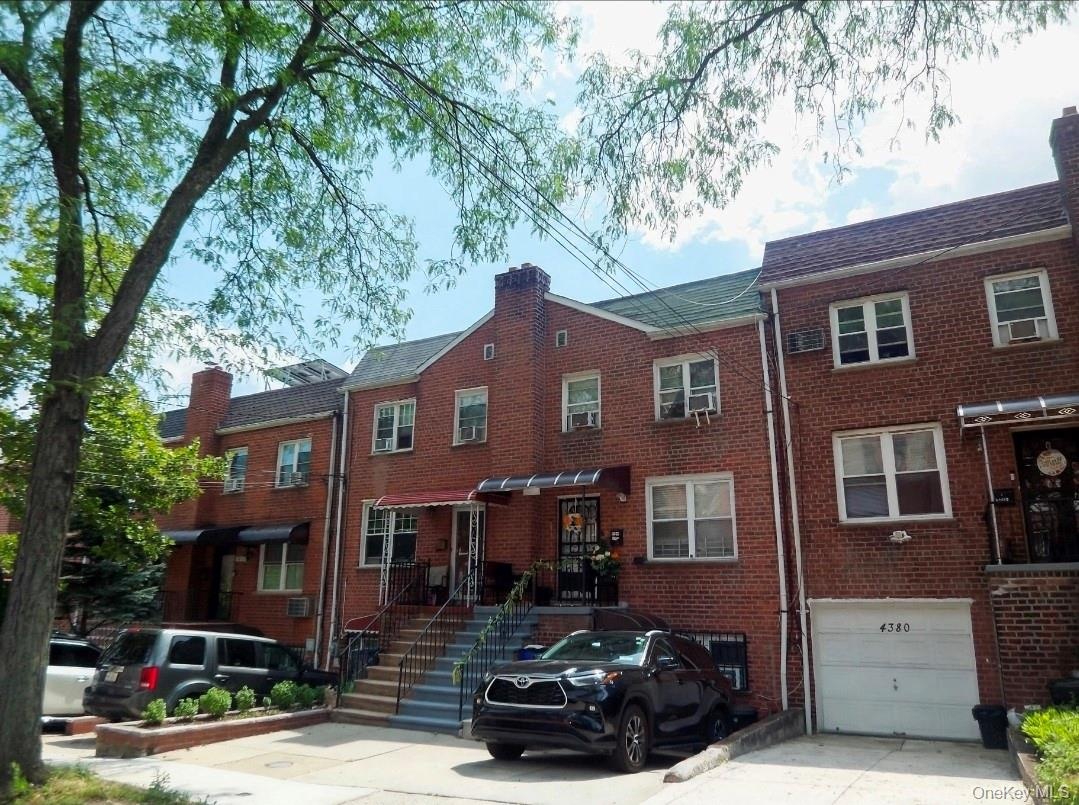 Brick rowhouse featuring a pitched roof, front entry awning, and a ground-level garage