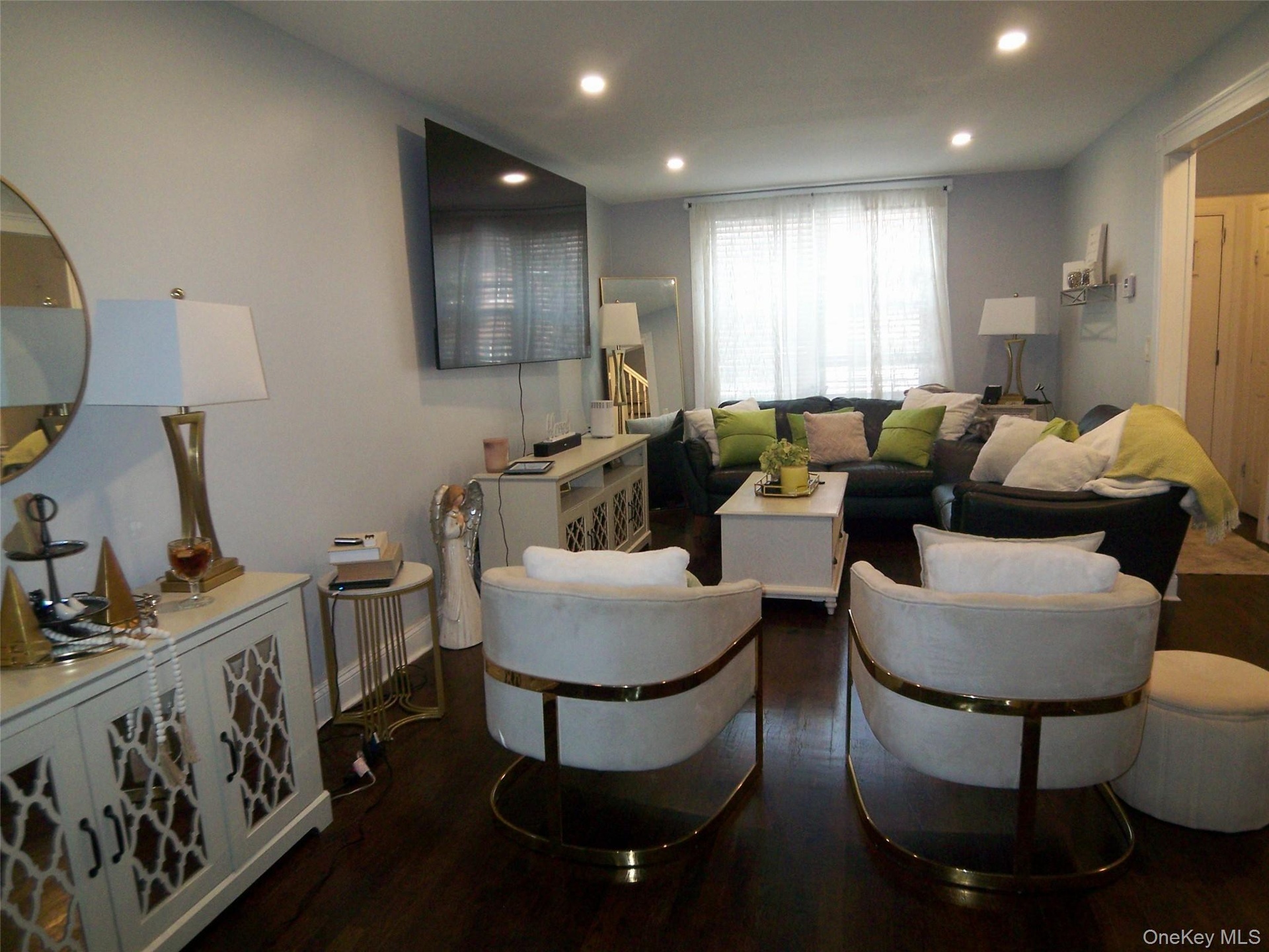 Spacious living area featuring dark wood-finish flooring, recessed lighting, and a large window with privacy blinds