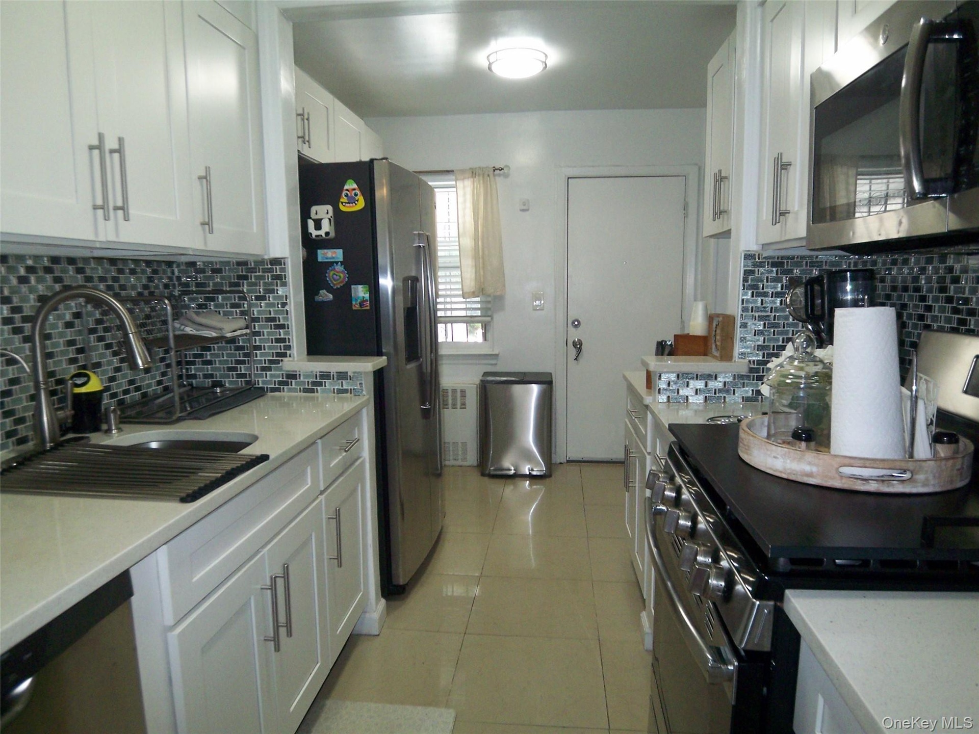 Galley kitchen featuring white cabinetry with brushed nickel pulls, light-toned countertops, and a mosaic tile backsplash