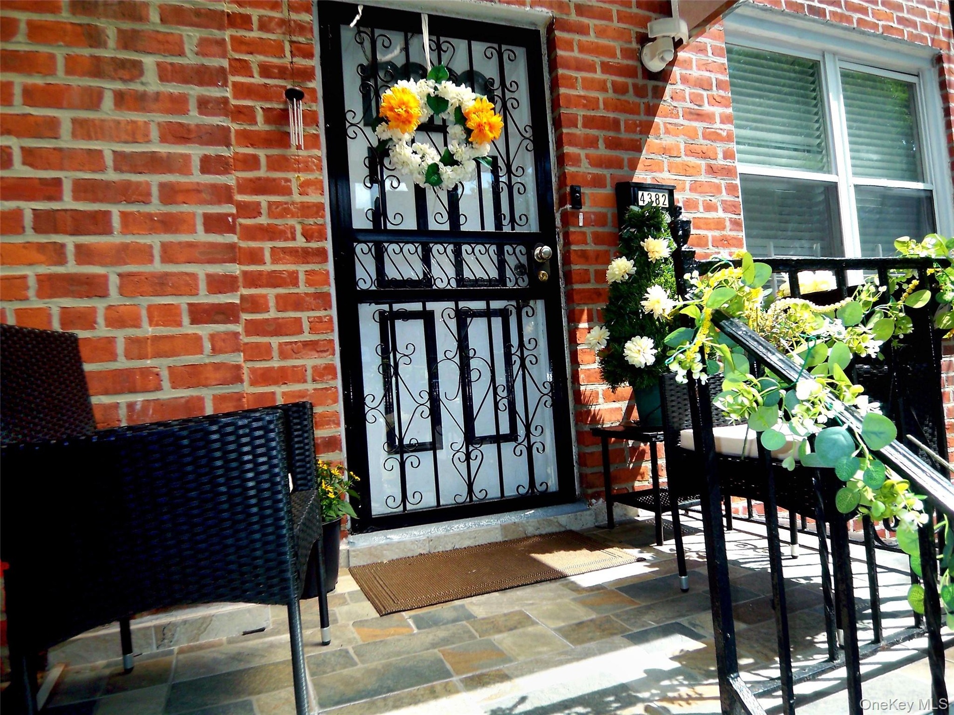 Brick facade entry featuring a black security door with scrollwork, multi-tone slate tile flooring, and a black wrought iron railing