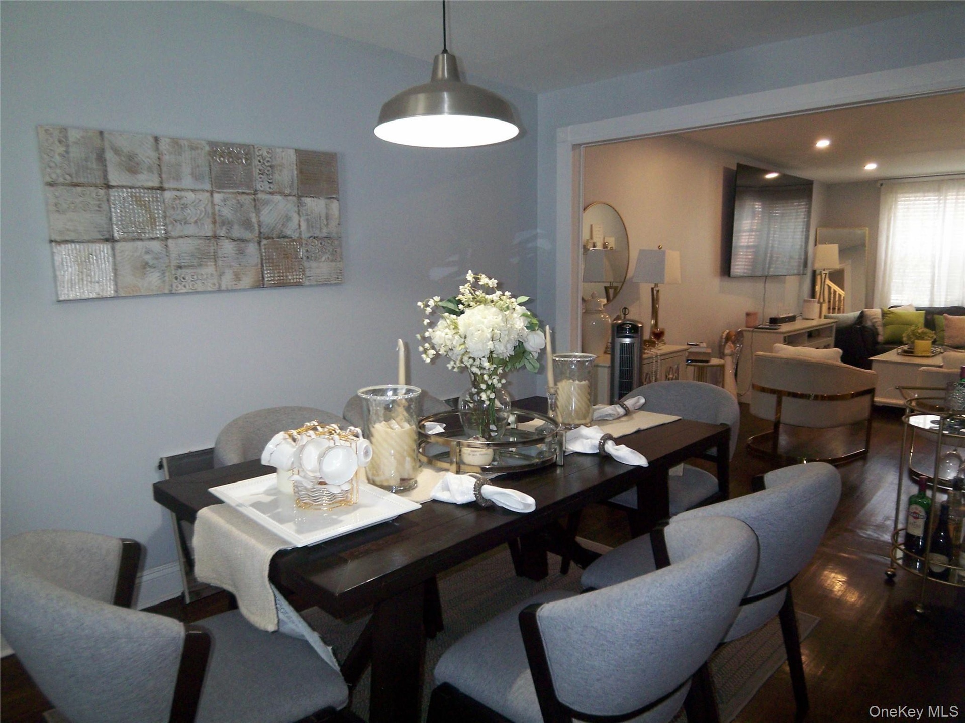 Dining area featuring dark wood-finish flooring, a contemporary pendant light fixture, and an open doorway to an adjacent living space