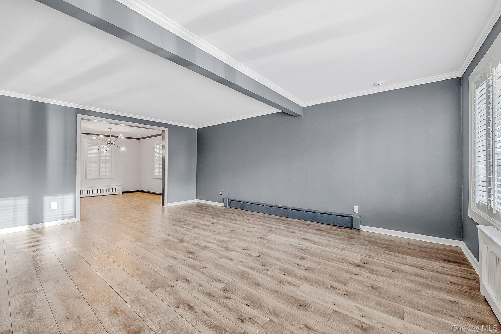 Unfurnished room with crown molding, light wood finished floors, a baseboard radiator, beam ceiling, and radiator