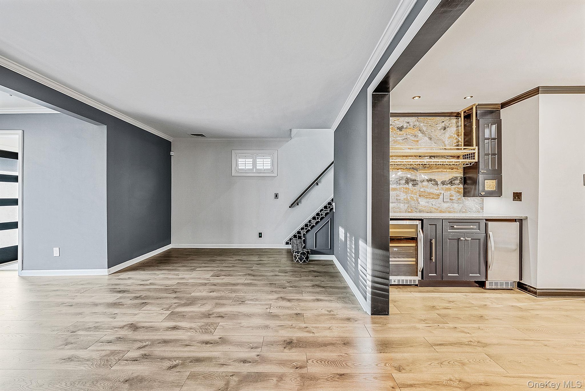 Indoor bar with stainless steel fridge, glass insert cabinets, ornamental molding, light wood-style flooring, and beverage cooler