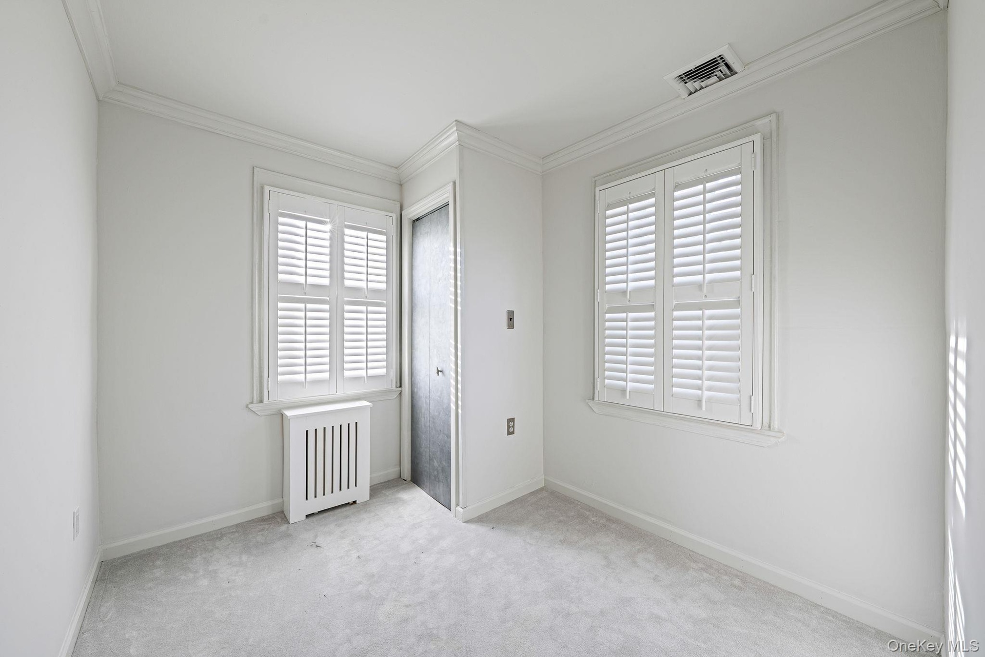 Unfurnished bedroom featuring radiator heating unit, crown molding, multiple windows, and carpet