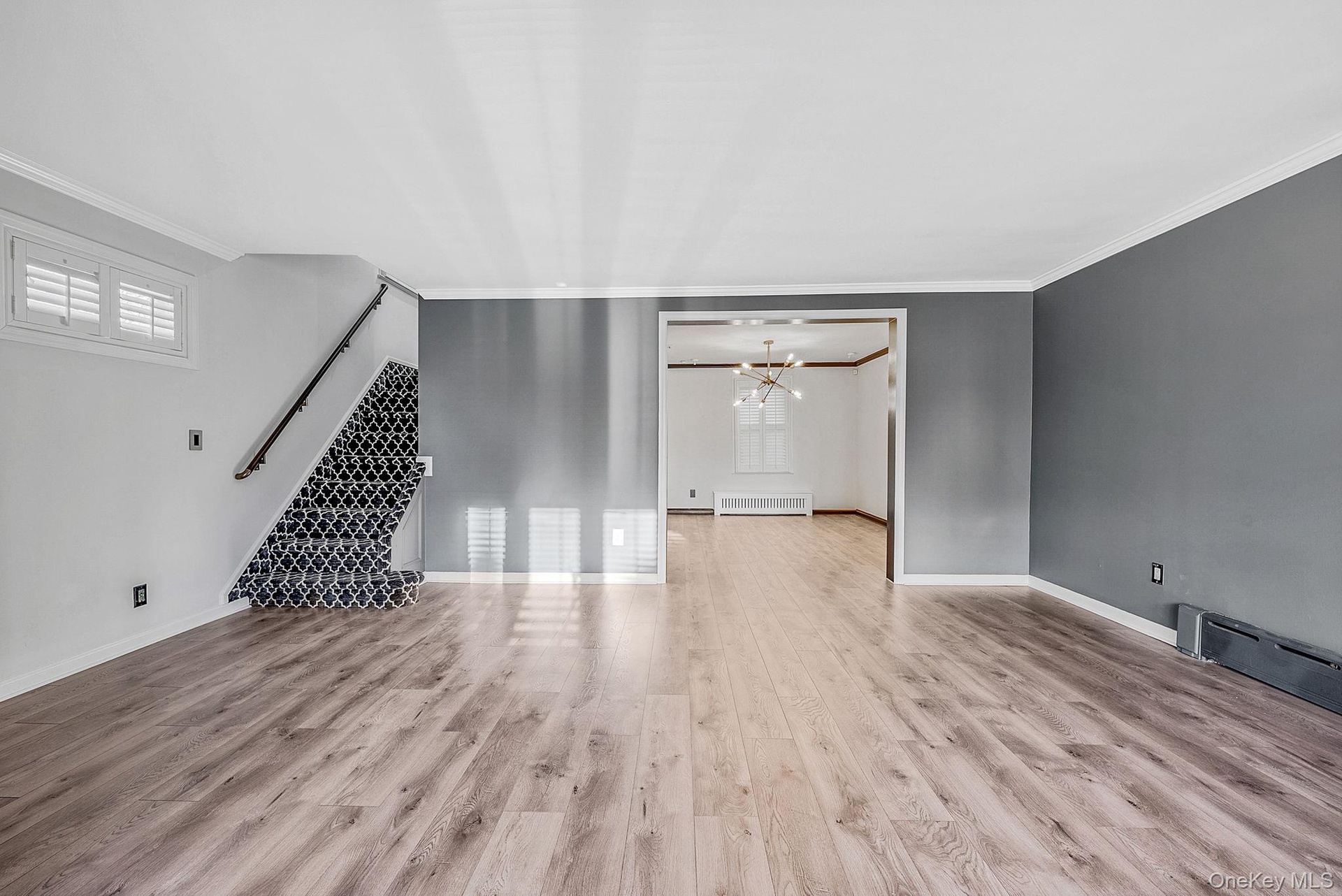 Unfurnished living room featuring a chandelier, light wood finished floors, crown molding, radiator heating unit, and a baseboard radiator