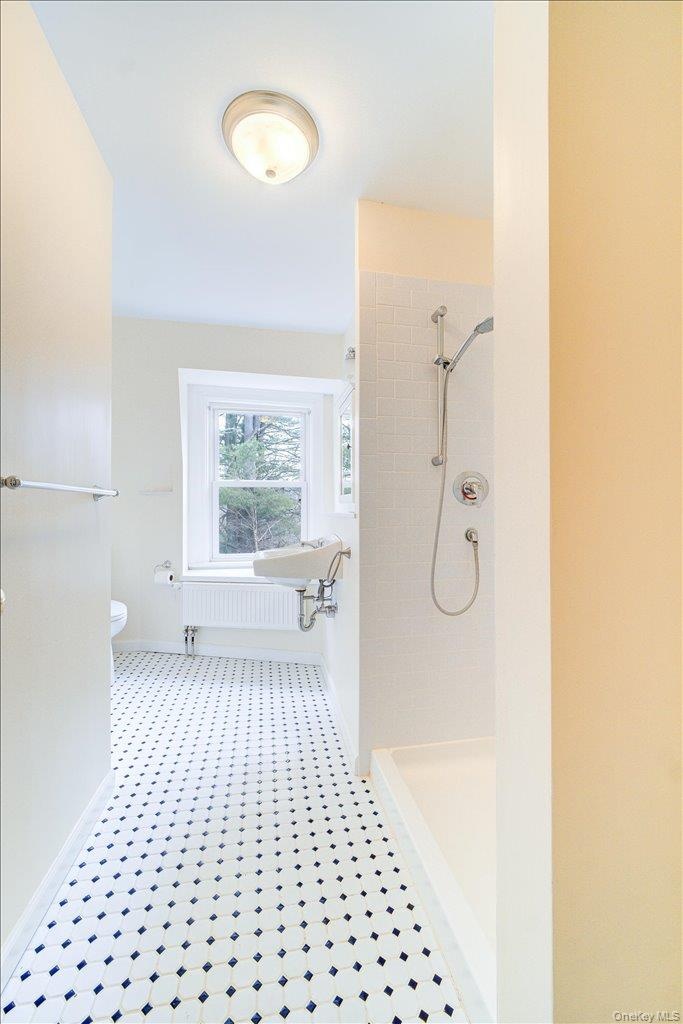 Bathroom with radiator heating unit, toilet, and tiled shower