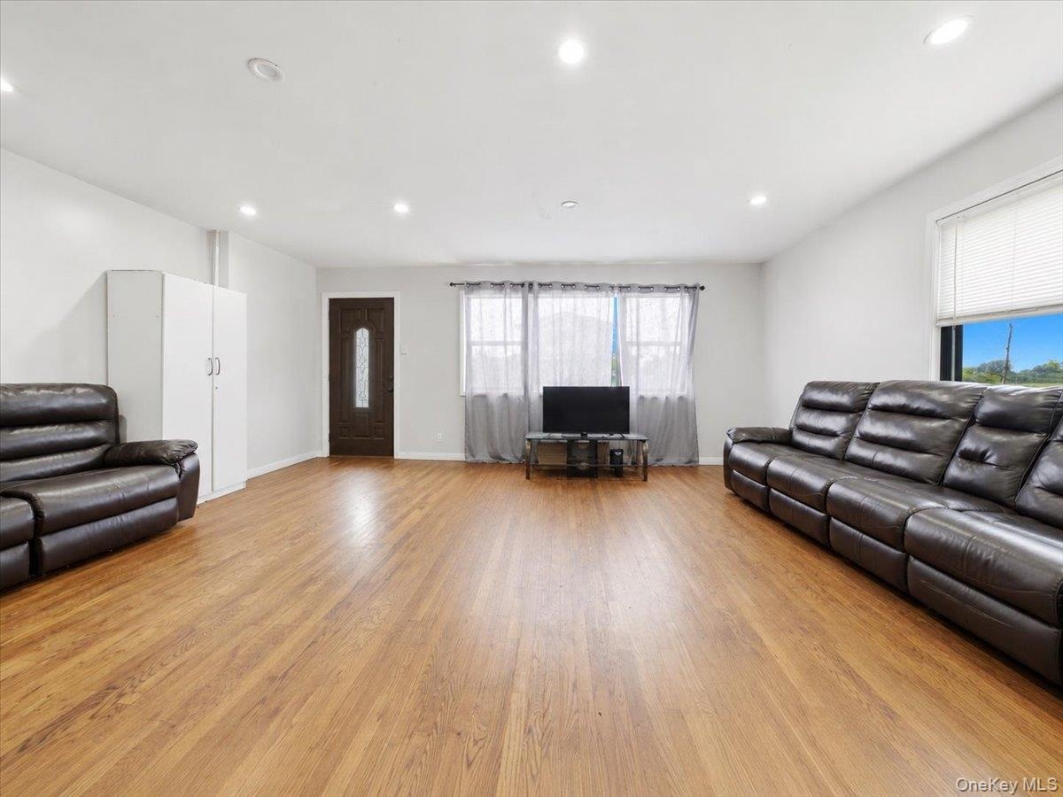 Spacious room featuring wood-finish flooring, recessed lighting, and a dark wood entry door with vertical glass insert