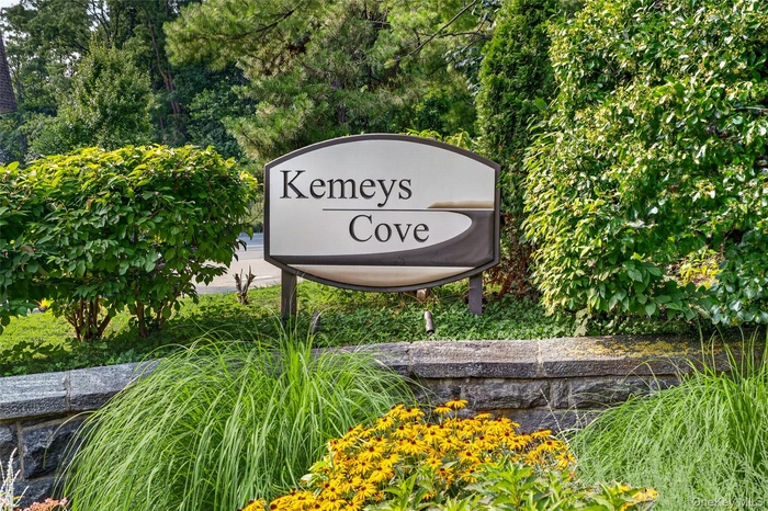 "Kemeys Cove" signage set within lush landscaping, featuring a stone retaining wall and vibrant yellow flowering plants