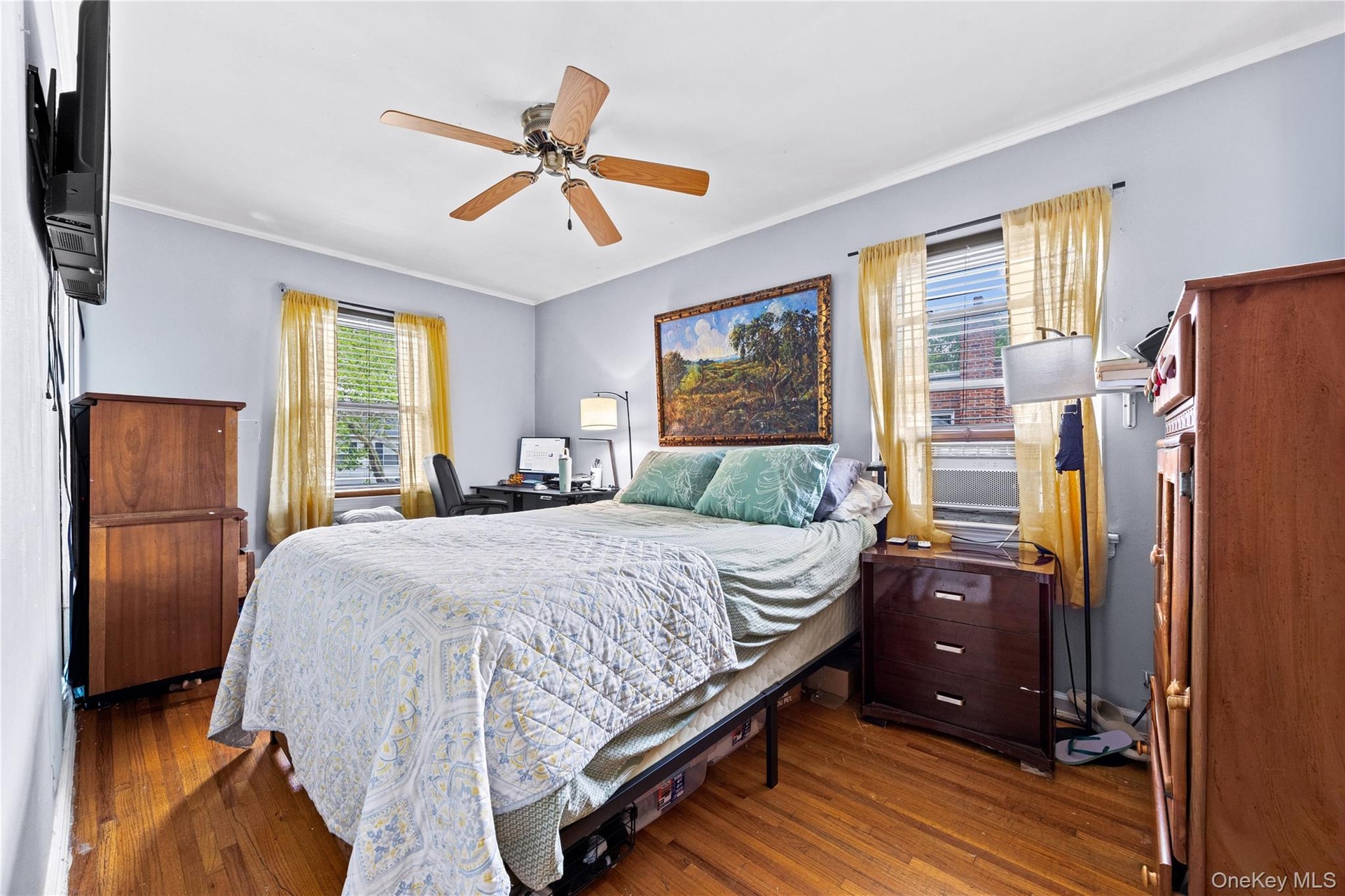Bedroom 3 - featuring wood-finish flooring, light blue walls, a ceiling fan with integrated lighting, and two windows with blinds