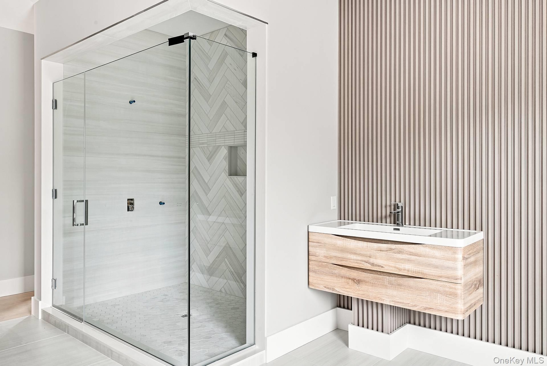 Spacious glass-enclosed shower with herringbone pattern tile accent wall and integrated niche