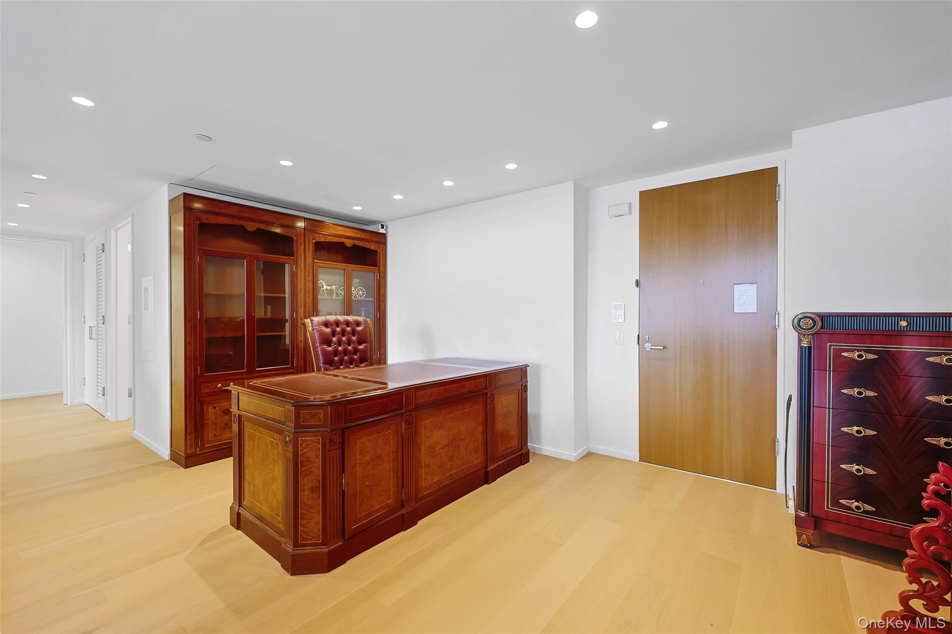 Recessed lighting illuminates wood-finish flooring and a built-in wall unit with glass-front cabinetry