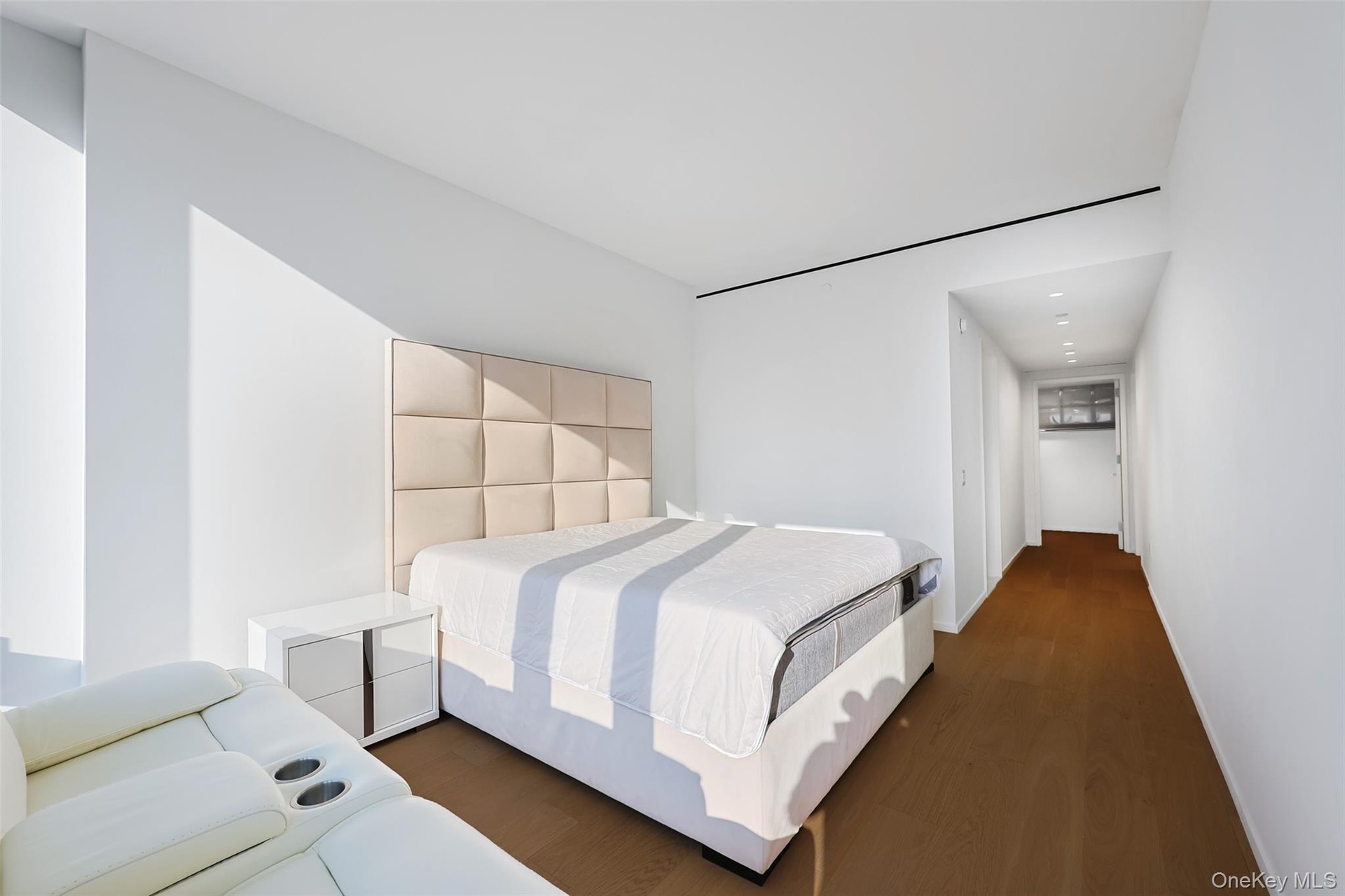 Bedroom featuring an upholstered headboard, white walls, wood-finish flooring, recessed lighting, and a linear ceiling light fixture