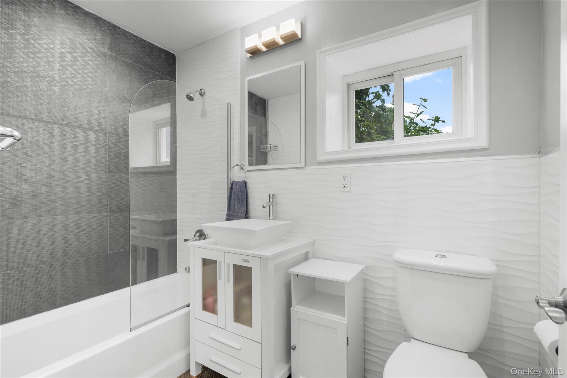 Bathroom featuring a white vanity with vessel sink, a shower-over-tub combination with glass partition.