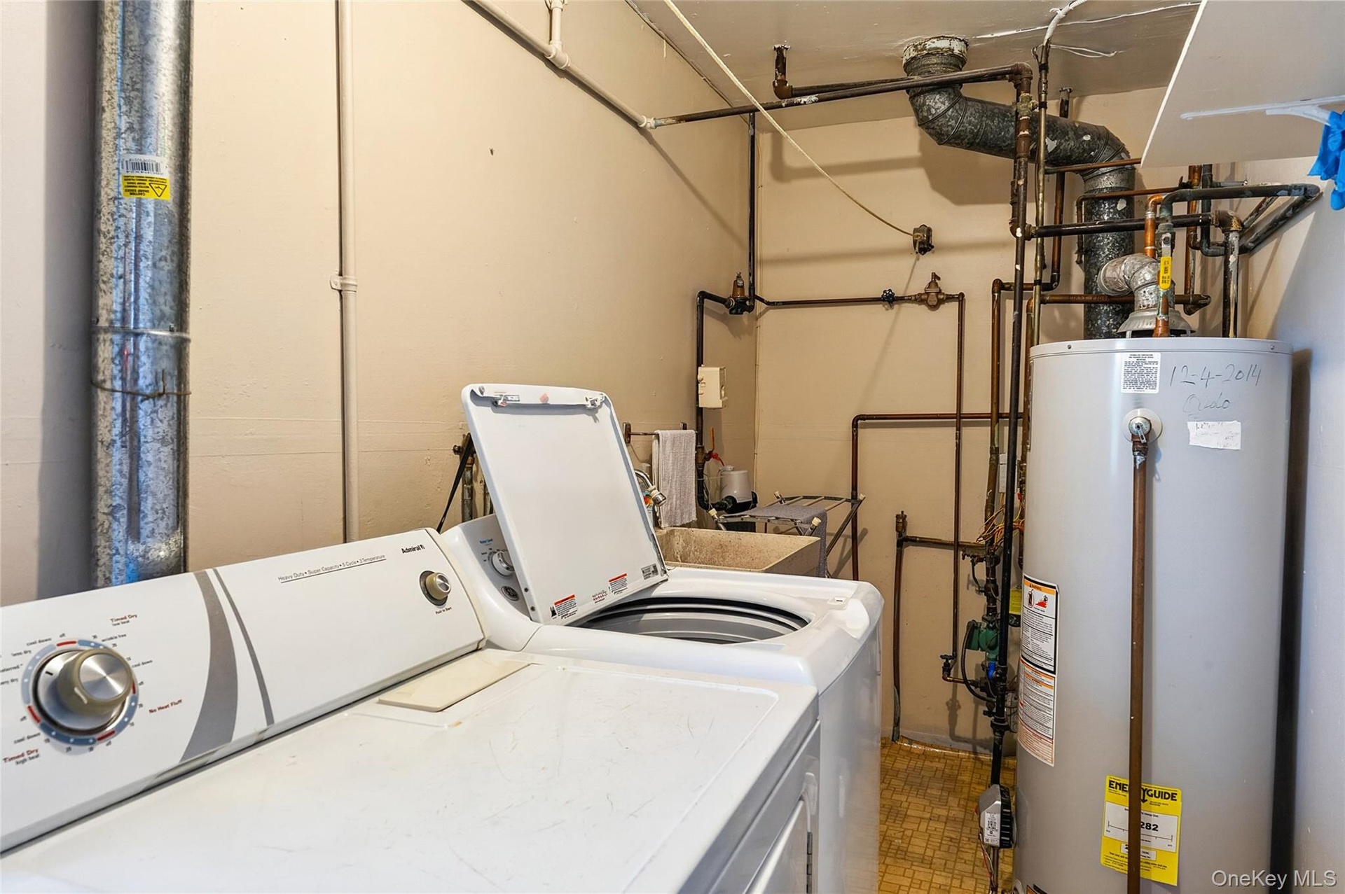 Utility area featuring a top-load washing machine, a water heater, a utility sink, exposed piping, and a large metal duct