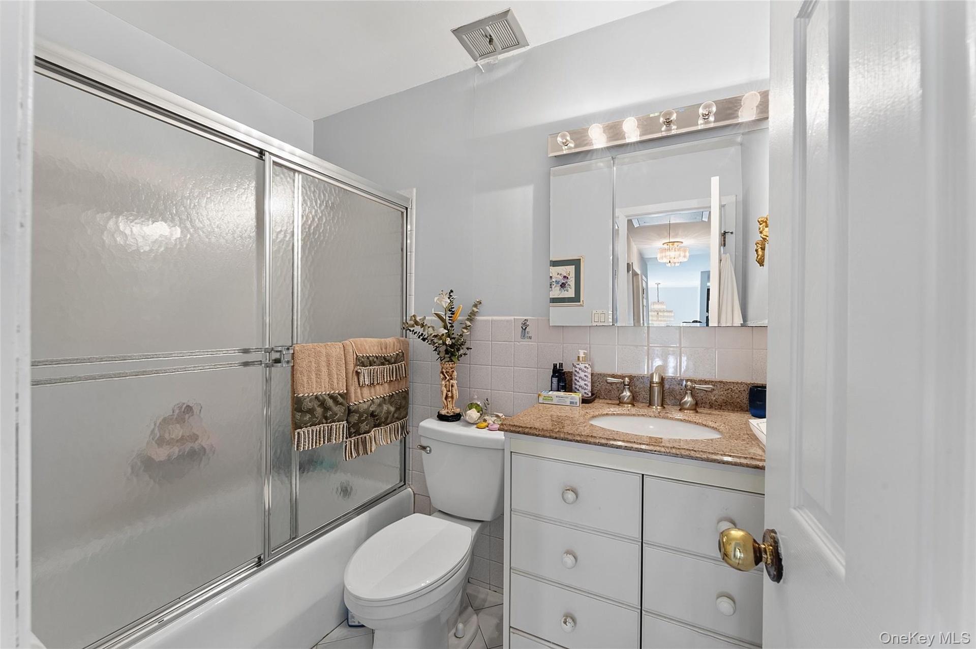 Bathroom featuring a shower/tub combination with sliding frosted glass doors, a vanity with a light-colored countertop and integrated sink, a mirrored