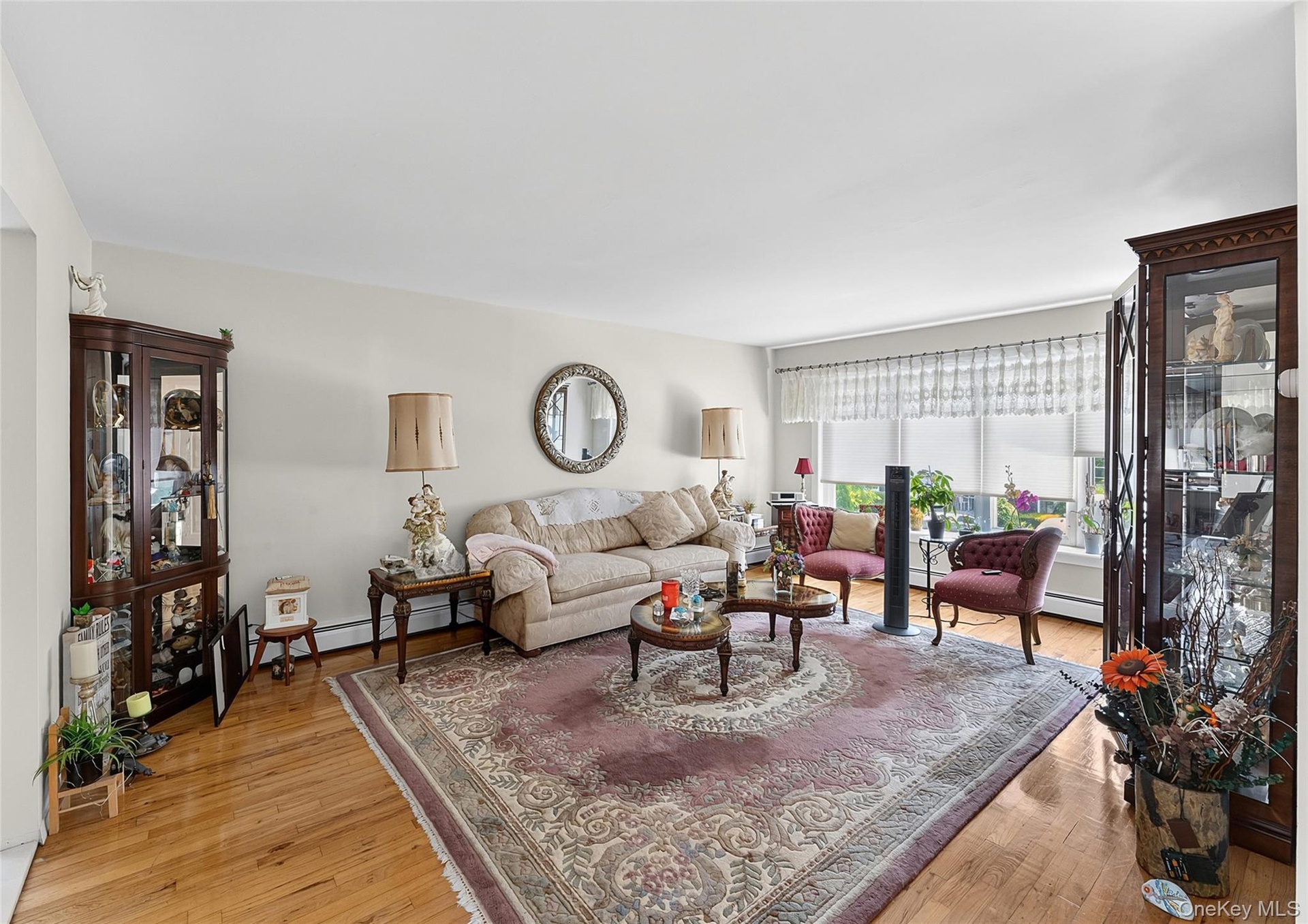 Spacious living area featuring polished wood-finish flooring, ample natural light from large windows, and neutral wall tones