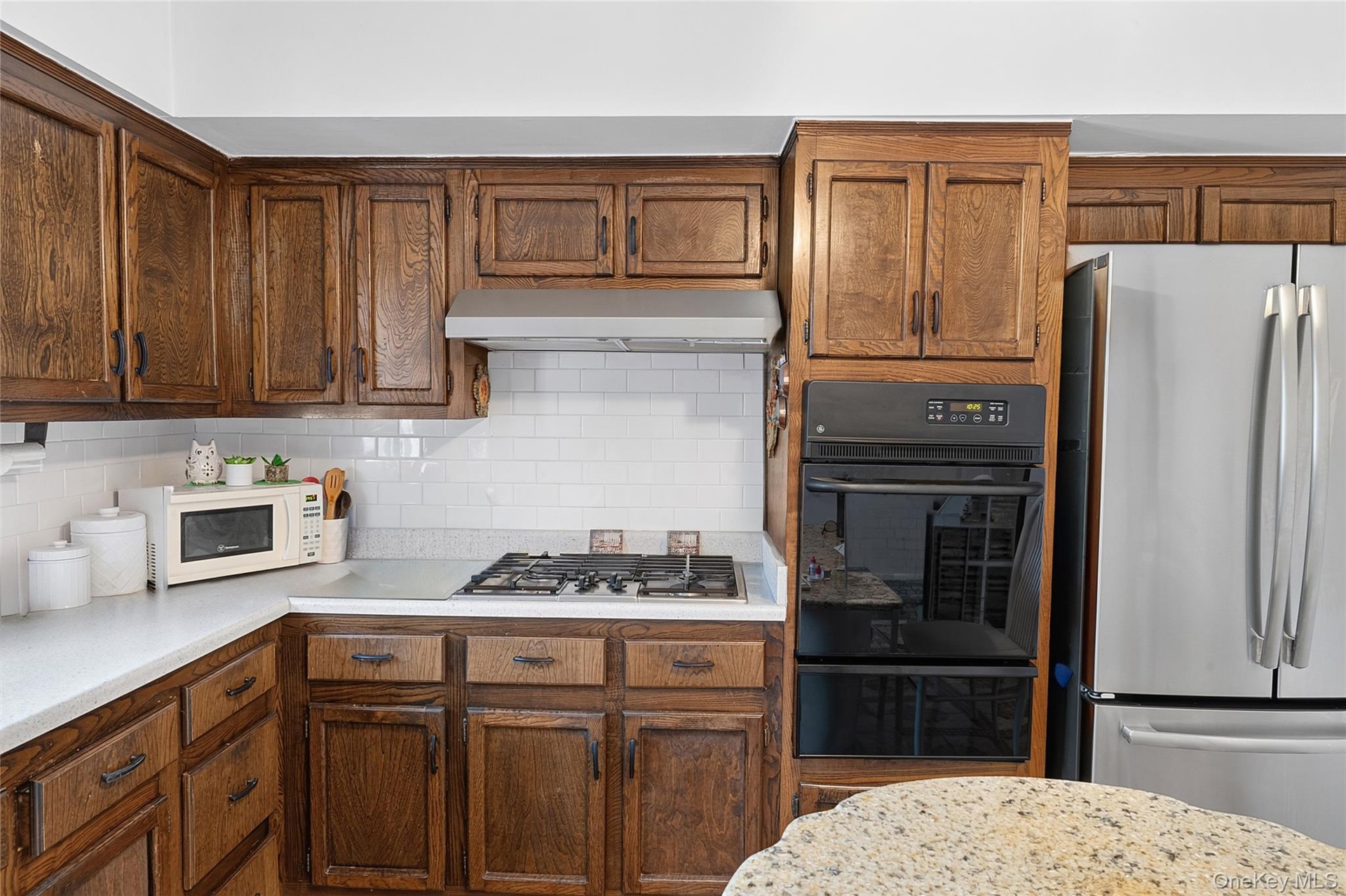 Kitchen featuring extensive wood cabinetry, white subway tile backsplash, white countertops, built-in gas range, and double wall ovens