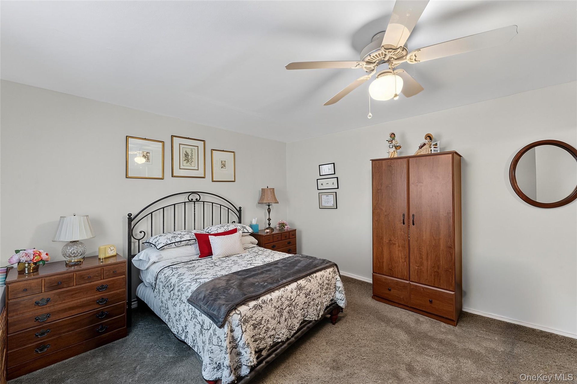 Carpeted bedroom featuring a ceiling fan with integrated lighting, a dark wood-finish armoire, and a rounded wall mirror