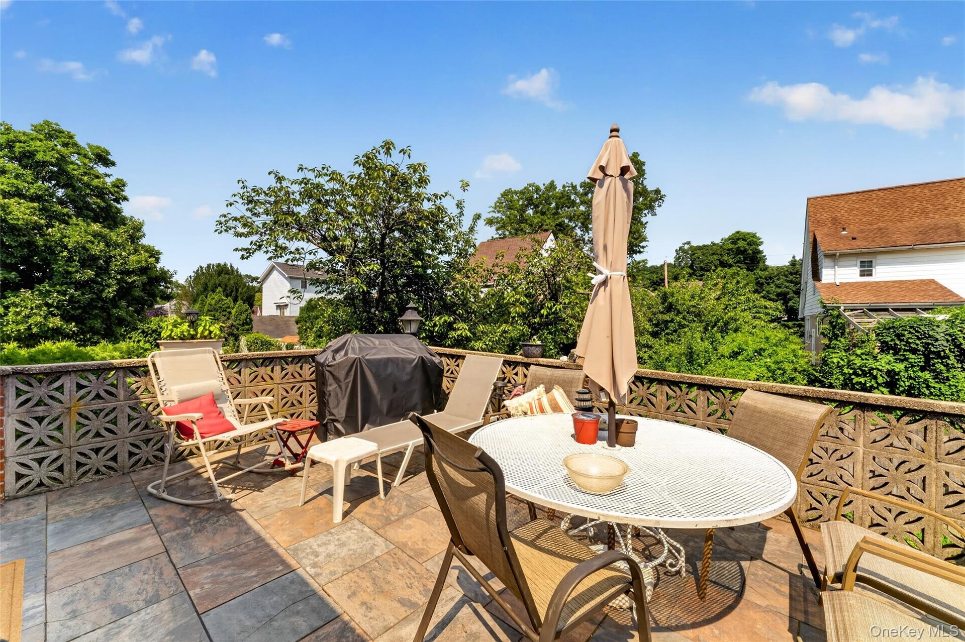 Expansive outdoor patio featuring flagstone flooring, a decorative block privacy wall, and mature perimeter trees
