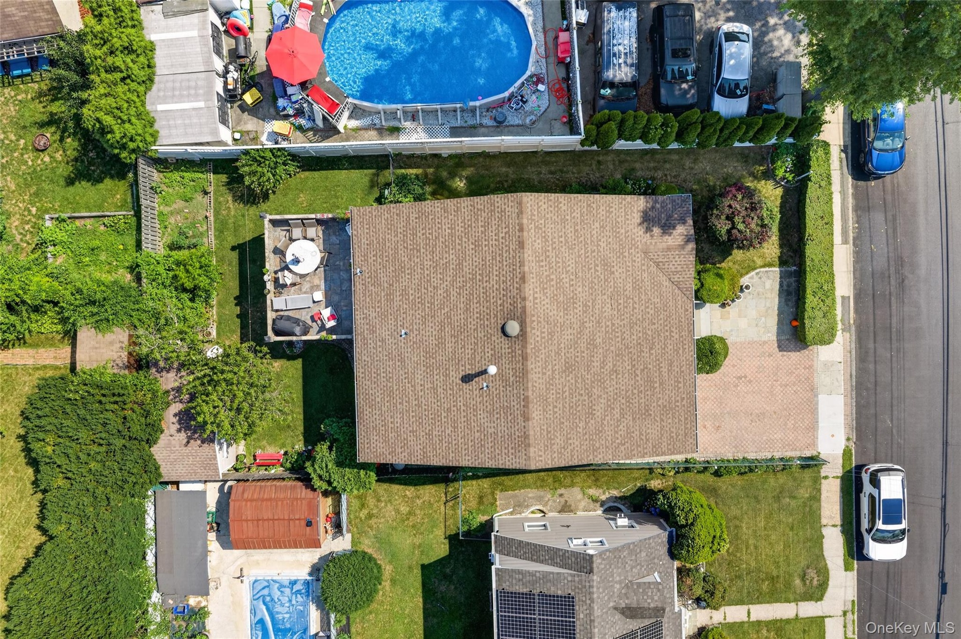 Brown shingle roof with a rear elevated patio, accompanied by a front paver driveway and mature landscaping