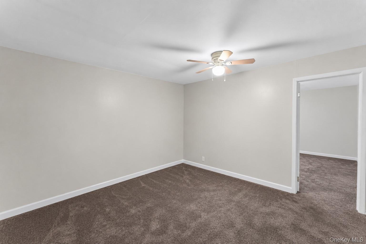 Spacious room featuring neutral wall paint, brown carpeting, and a ceiling fan with light fixture