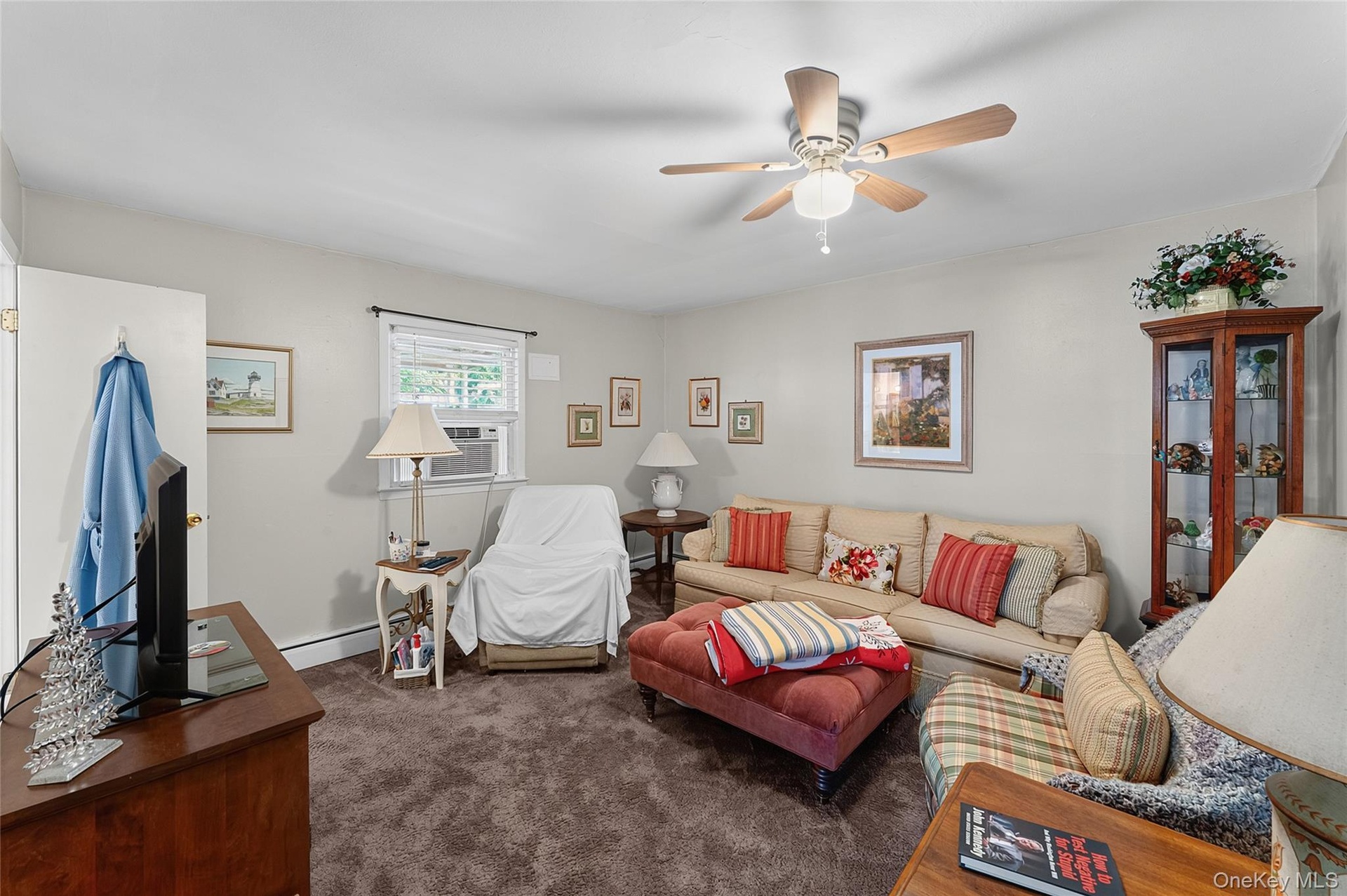 Carpeted living area featuring a ceiling fan with light fixture, window with blinds, and white painted walls