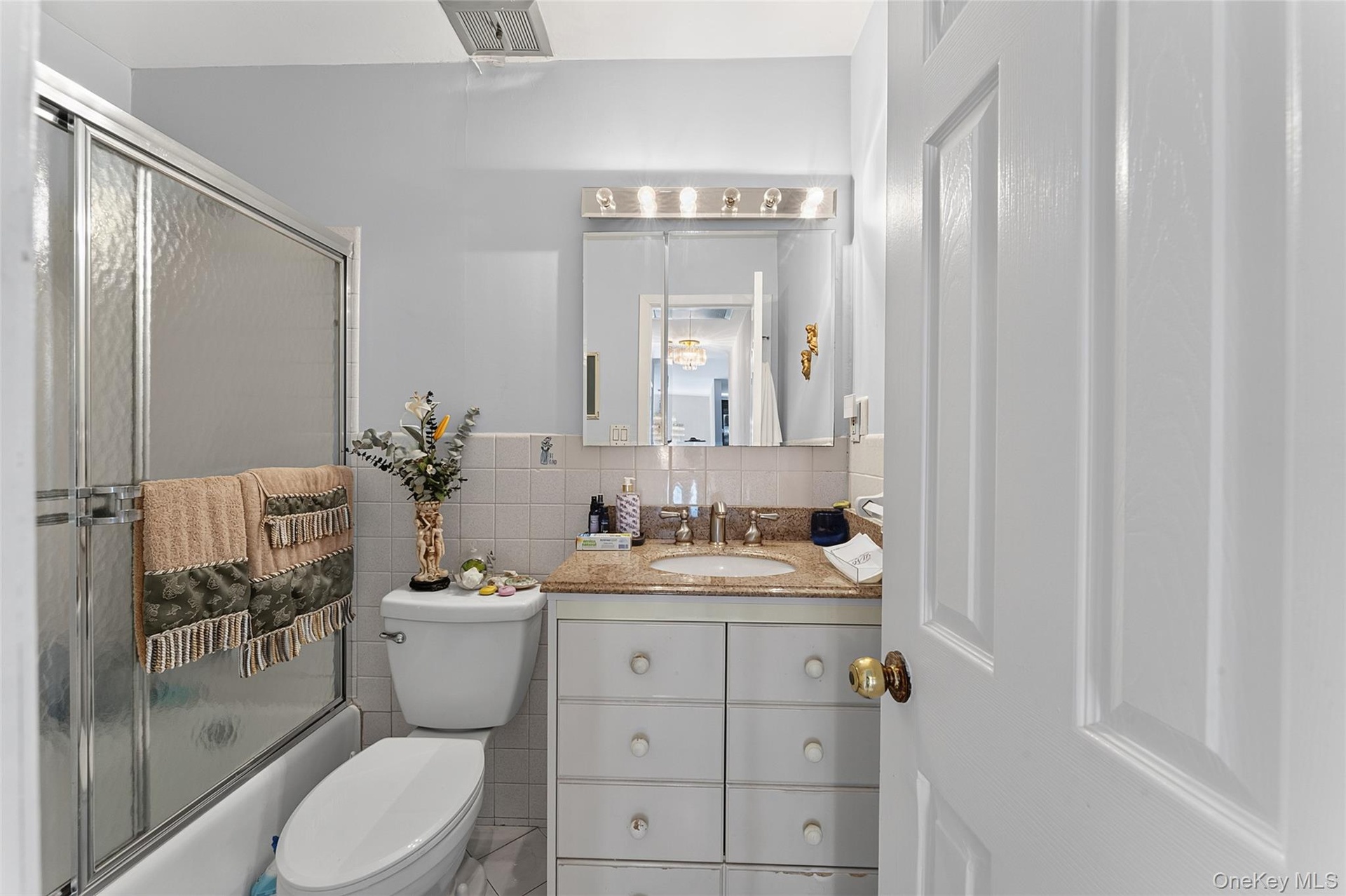 Bathroom featuring a tub/shower combination with sliding glass doors, a vanity with a light-colored countertop, and a mirrored medicine cabinet with o