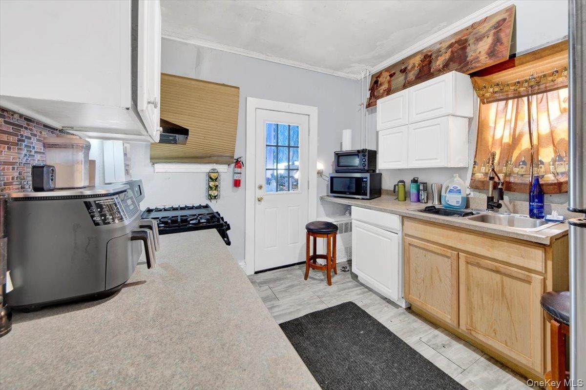 Kitchen with light countertops, black range with gas stovetop, stainless steel microwave, white cabinetry, and light brown cabinetry