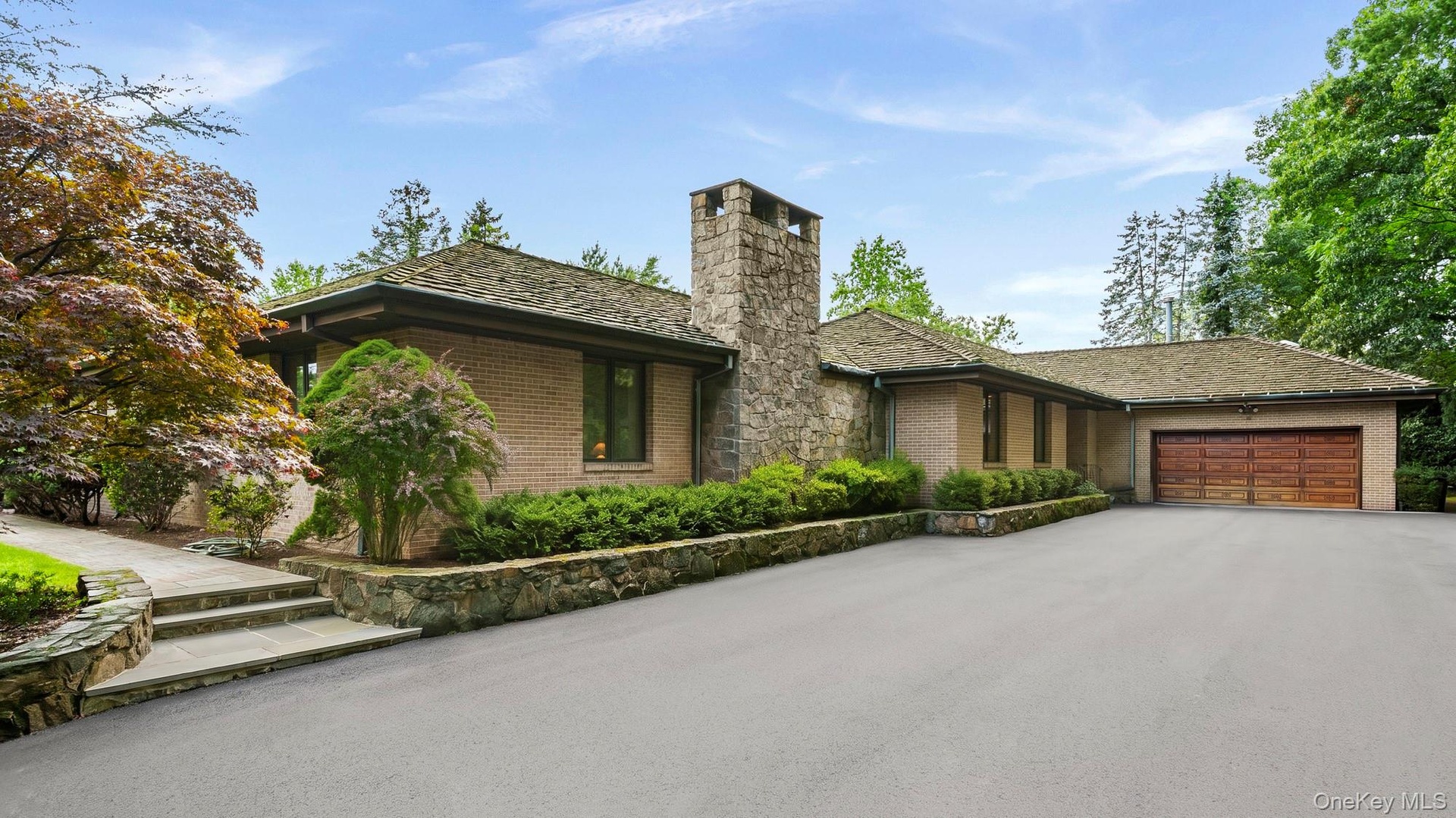 Mid Century style Ranch showcasing a low-pitched roof line, prominent stone chimney, and multi-car driveway.