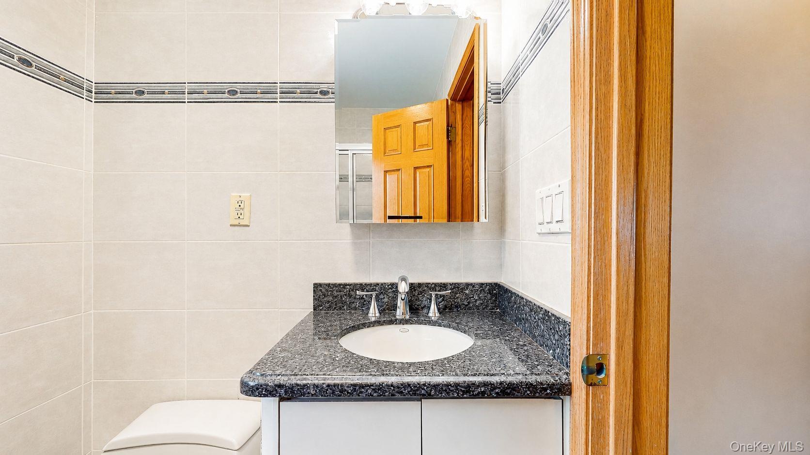 Bathroom vanity featuring a dark speckled countertop with an undermount sink and chrome faucet