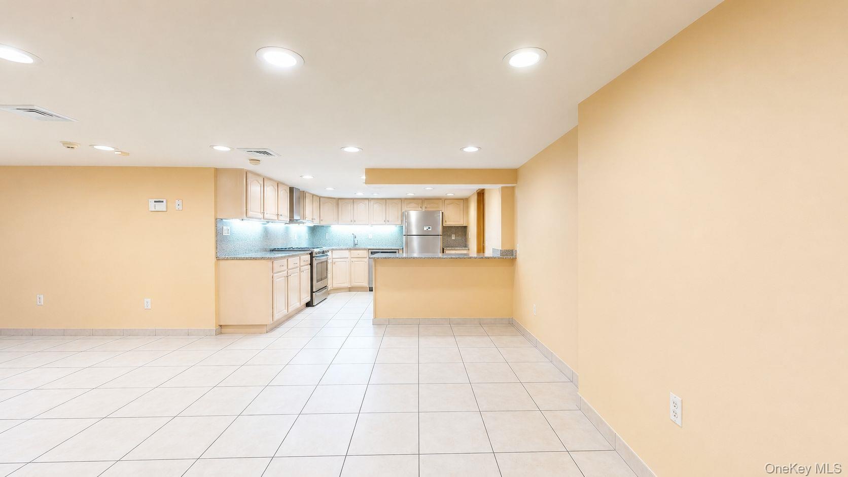 Open-concept living area featuring a kitchen with light wood cabinetry, stainless steel appliances, a breakfast bar, and recessed lighting
