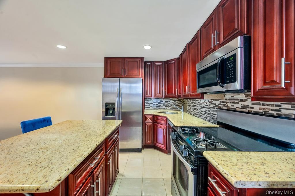 Kitchen featuring rich wood-finish cabinetry, light speckled countertops, stainless steel appliances, and a mosaic tile backsplash