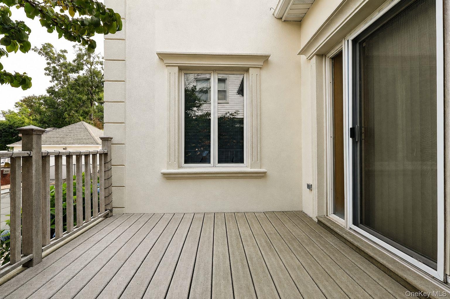 Outdoor deck featuring composite decking, a wooden railing, a sliding glass door, and an exterior window with decorative molding