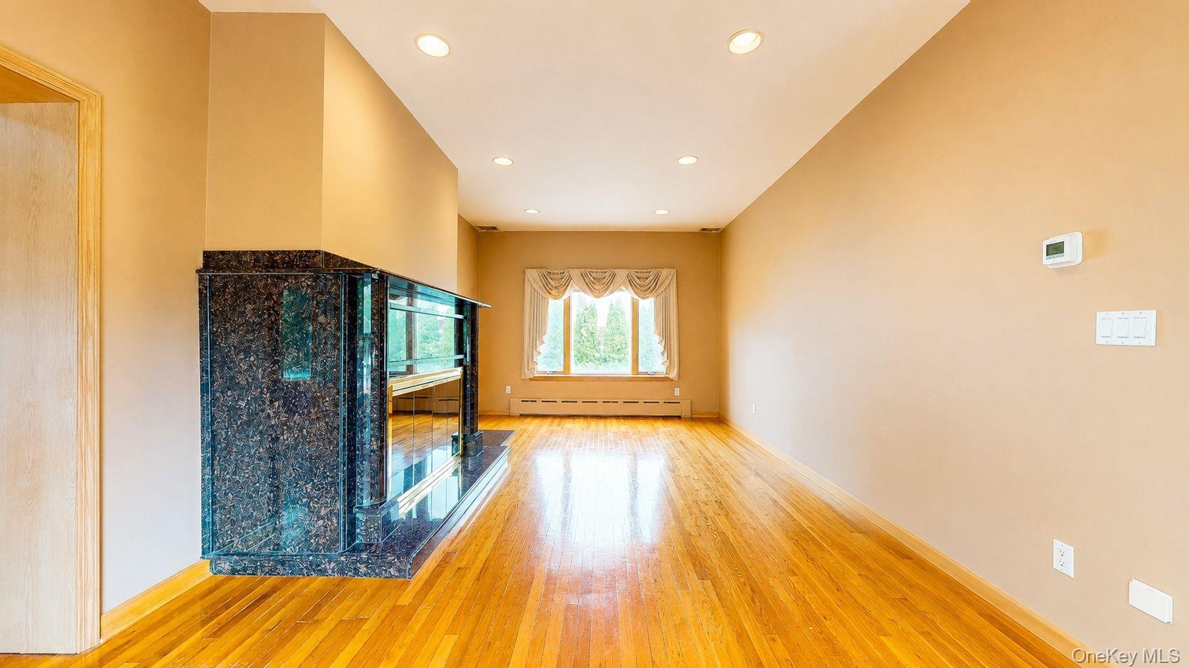 Spacious room featuring wood-finish flooring, recessed lighting, and a built-in dark granite-look fireplace with a hearth