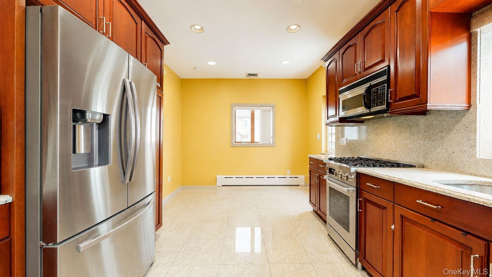 Galley kitchen featuring wood cabinetry, stainless steel appliances, recessed lighting, polished tile flooring, and light-toned countertops with match