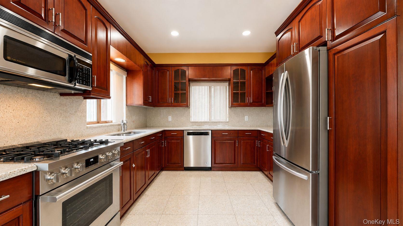U-shaped kitchen featuring wood cabinetry, stainless steel appliances, speckled countertops, and a tile backsplash