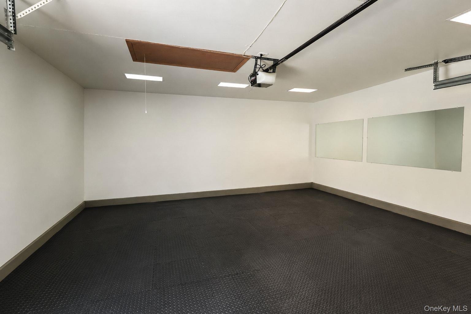 Spacious garage featuring textured black flooring, white painted walls, recessed lighting fixtures, and an automatic garage door opener mechanism