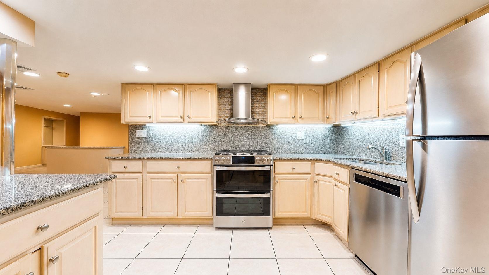 Kitchen featuring light wood cabinetry, stainless steel appliances, granite countertops, and tile flooring