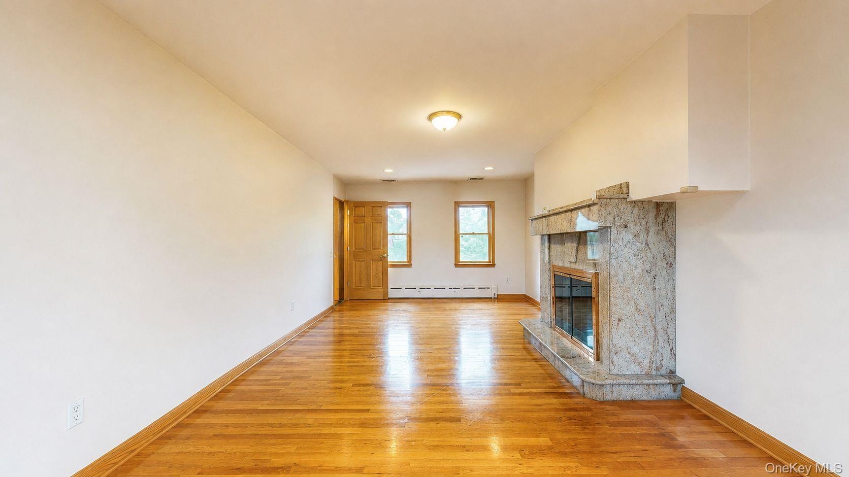 Expansive room featuring rich wood flooring, a decorative fireplace with a substantial stone surround and hearth, multiple windows, and a wood-panel d
