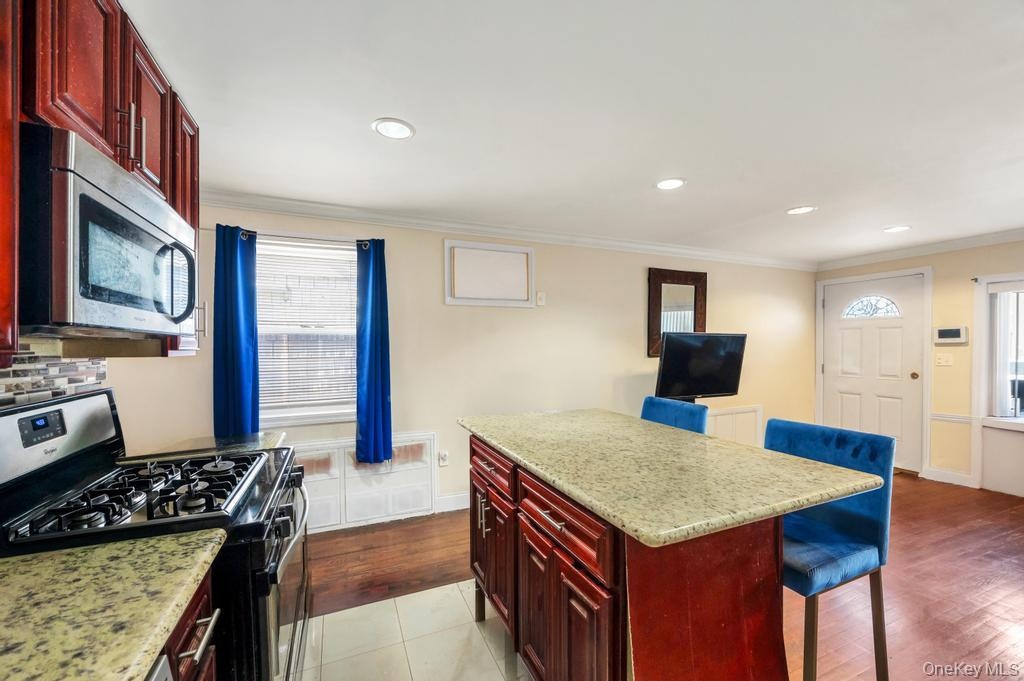 Kitchen featuring a gas range, stainless steel microwave, cherry wood-finish cabinetry, granite-style countertops, and a tile backsplash