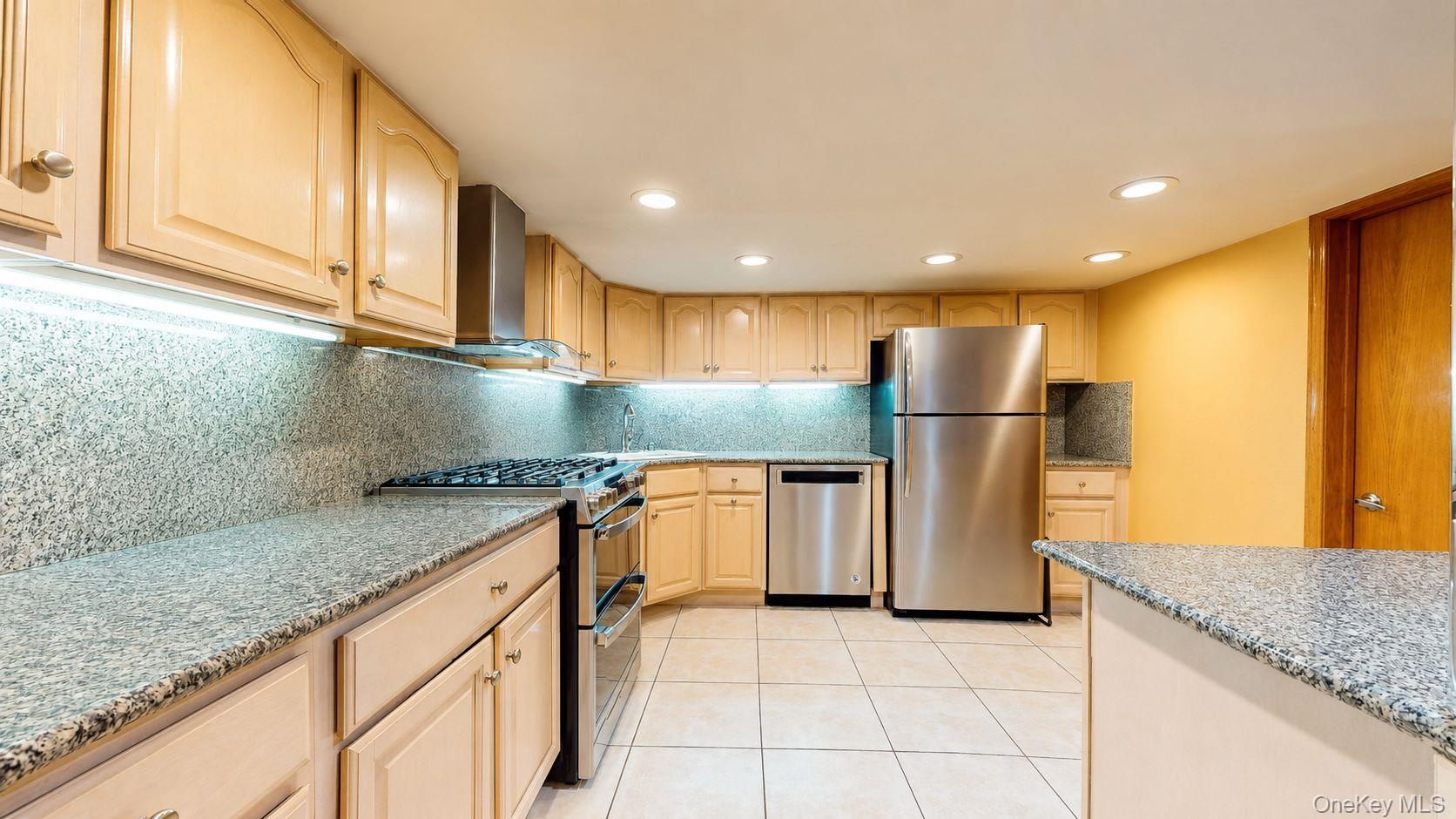 Kitchen featuring extensive light wood cabinetry, stone countertops, integrated stainless steel appliances, recessed ceiling lighting, and tiled floor