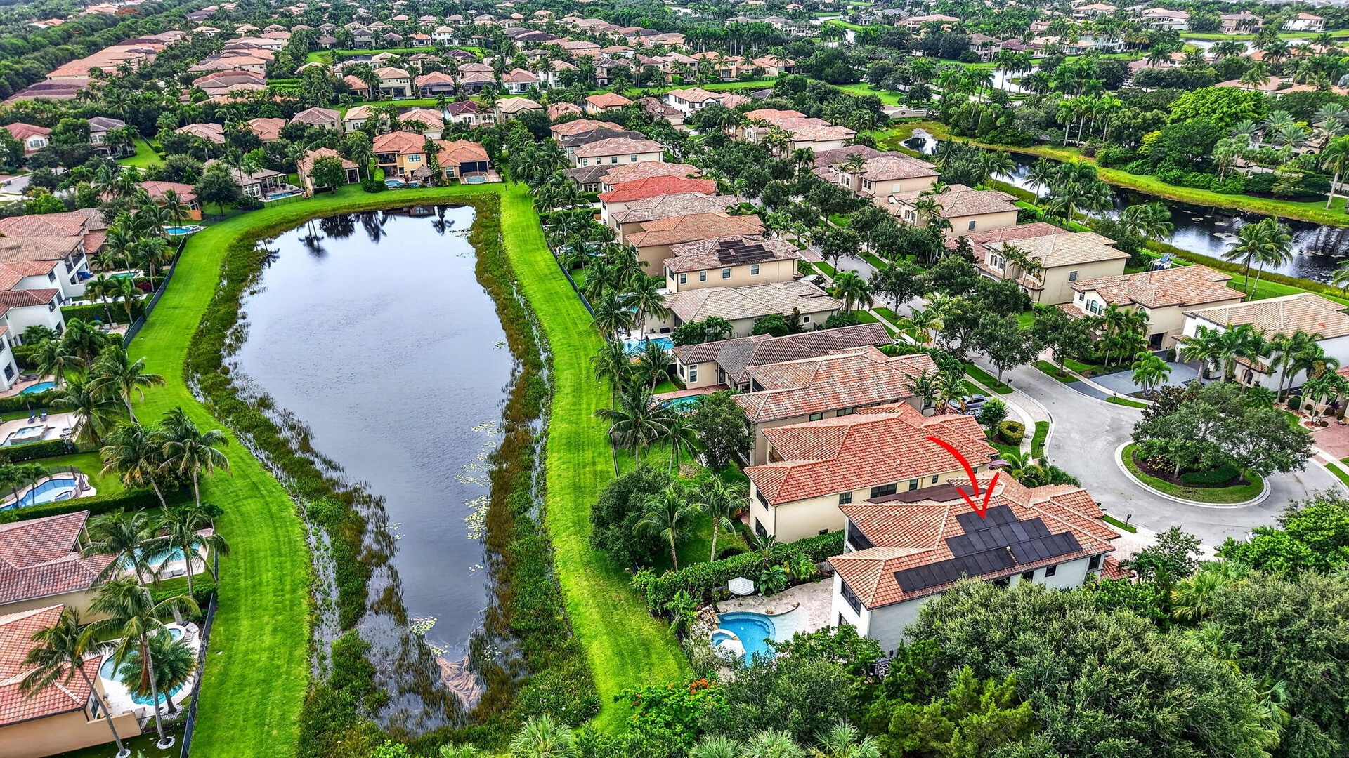 Aerial view showcasing a residential property with solar panels and a private pool, positioned along a water feature