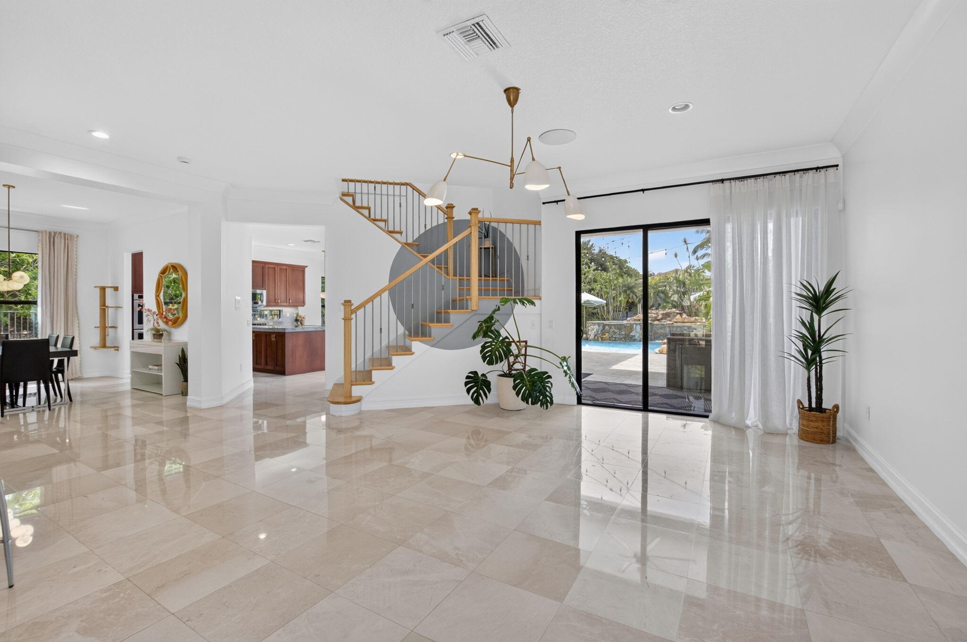 Expansive main living area featuring polished tile flooring, a contemporary chandelier, a staircase with wood newel posts and metal spindles, and larg