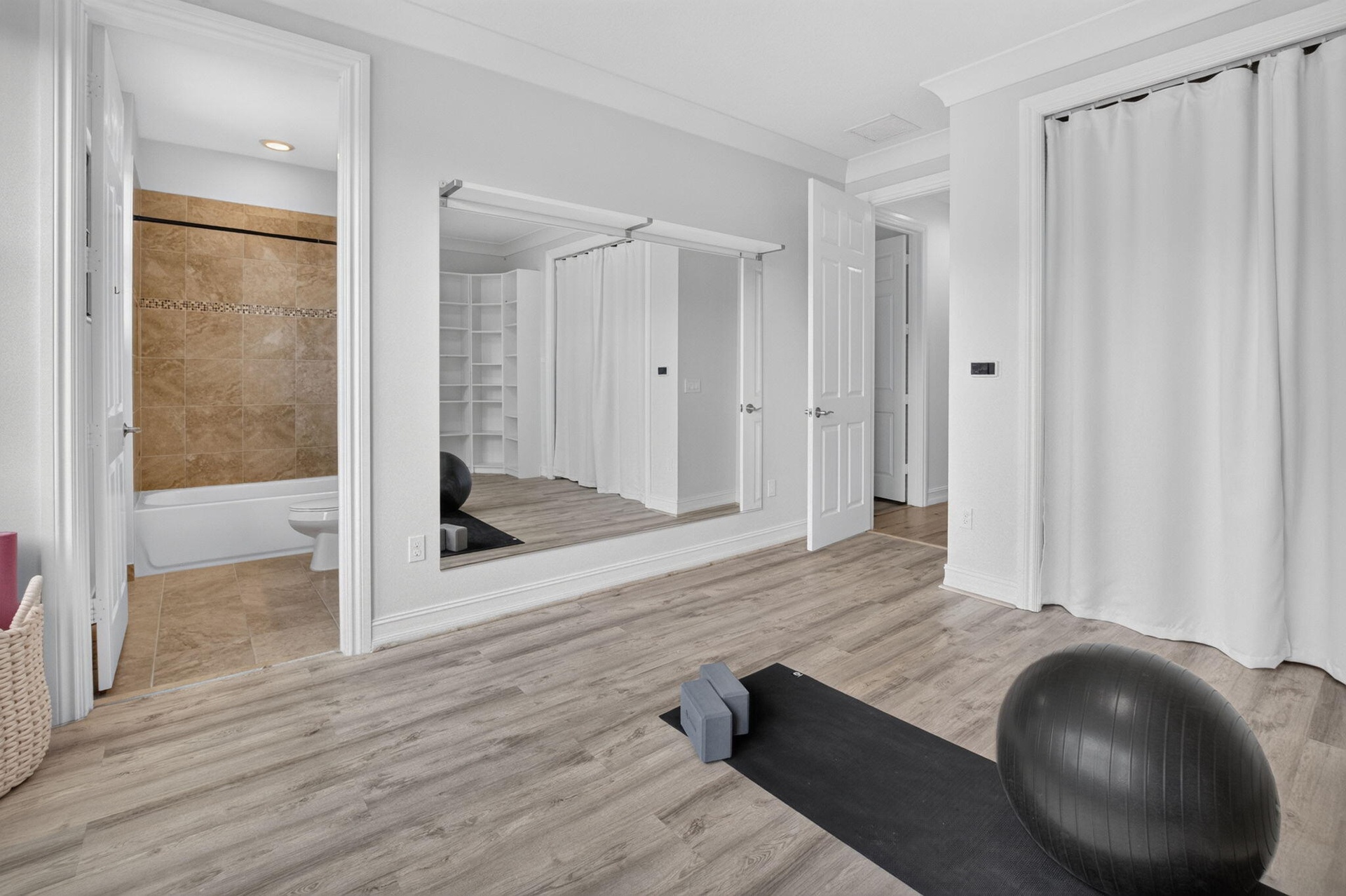 Room featuring wood-finish flooring, full-wall mirror, and a privacy curtain covering a built-in storage area