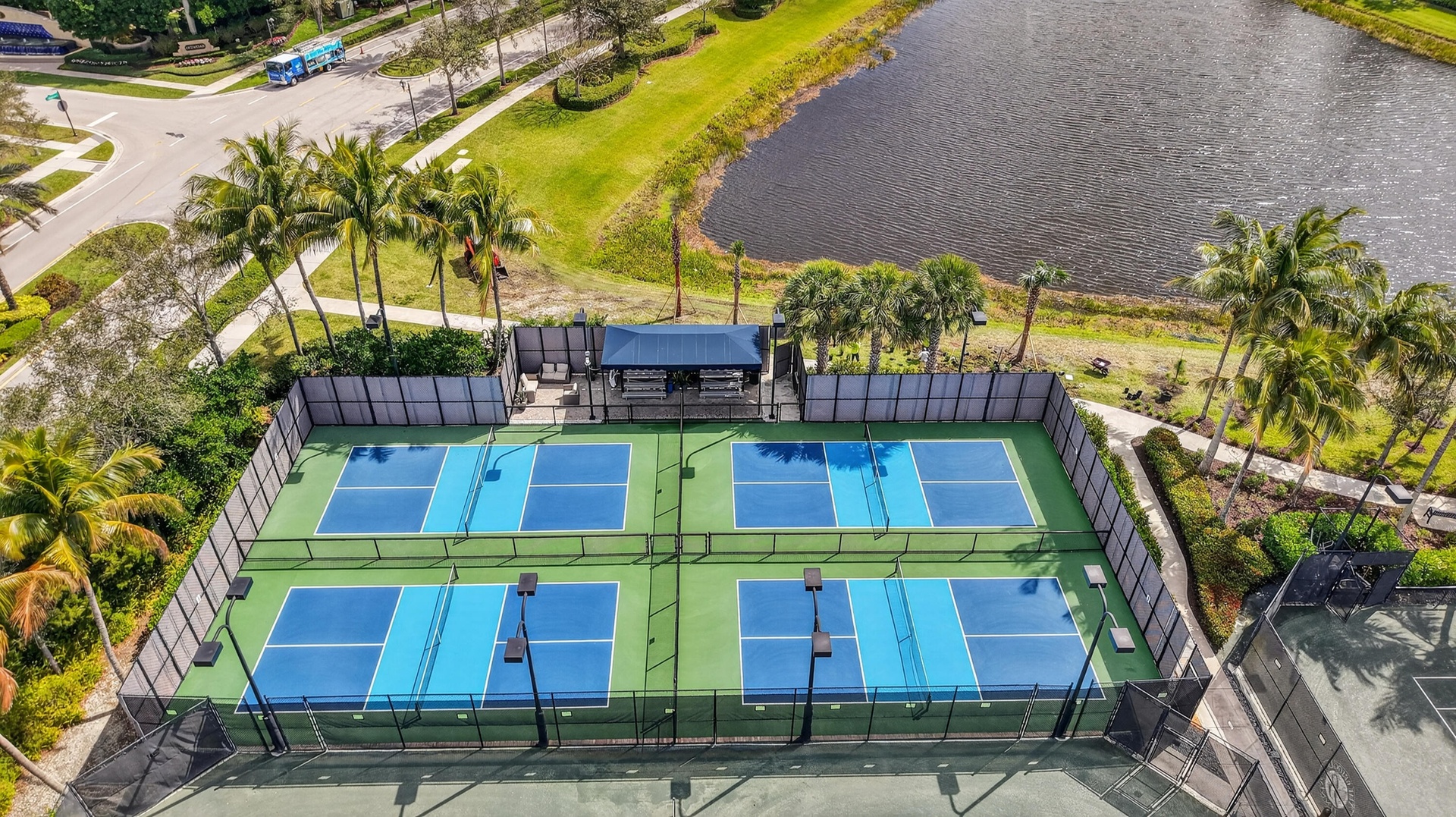 Four outdoor pickleball courts with blue and light blue playing surfaces, surrounded by fencing