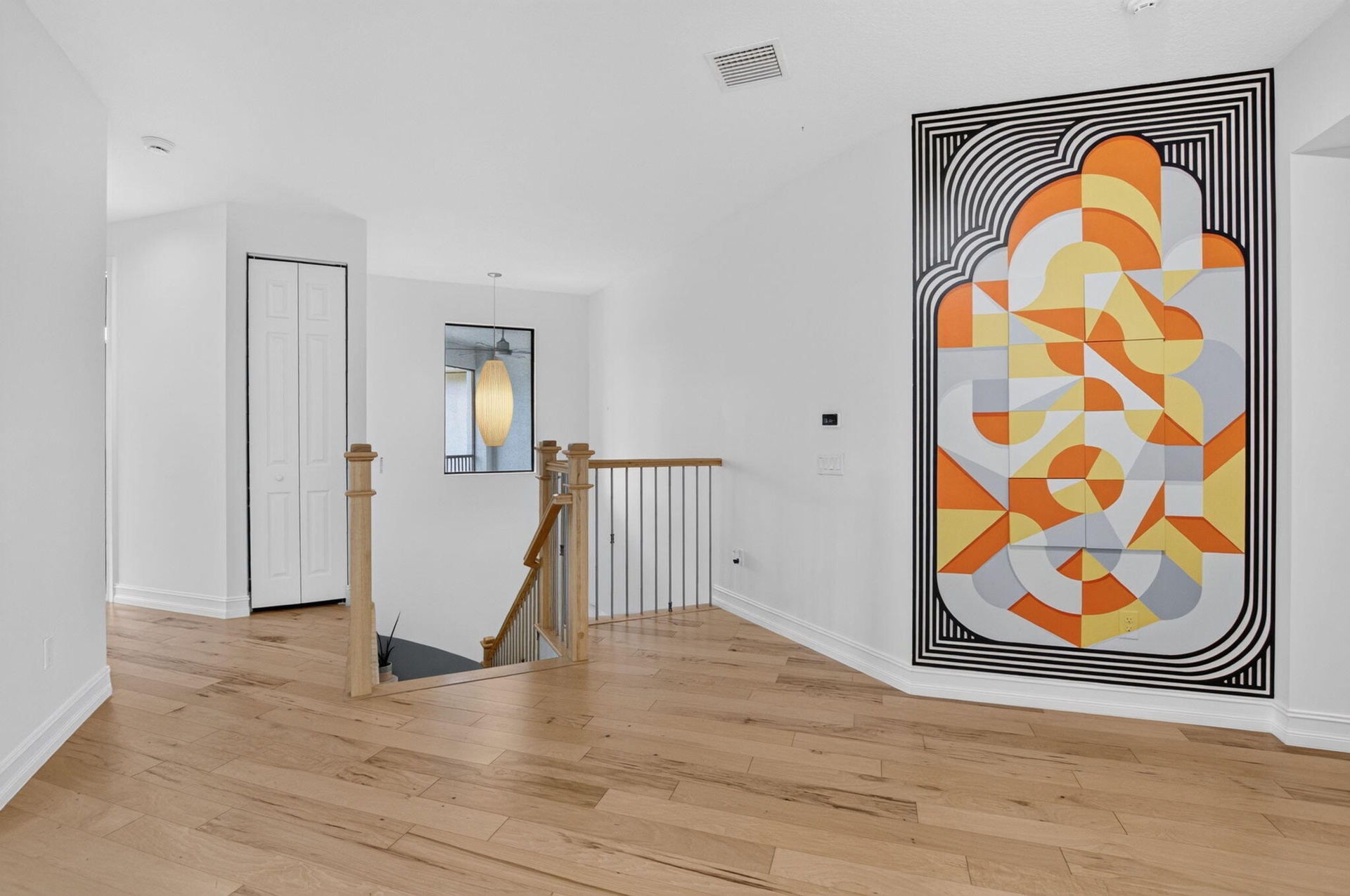 Expansive hallway with light wood-finish flooring, white walls, and a contemporary pendant light fixture